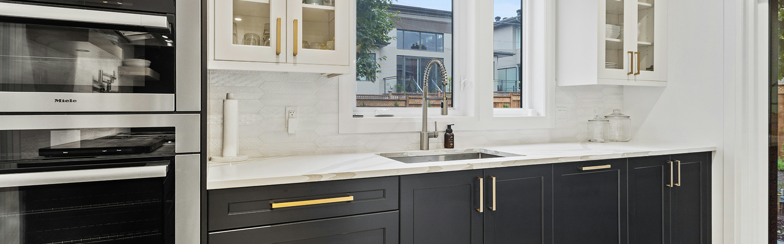 Modern kitchen with sleek black and white cabinetry, stainless steel appliances, and a polished countertop, showcasing a functional and stylish design ideal for cabinet painting services.