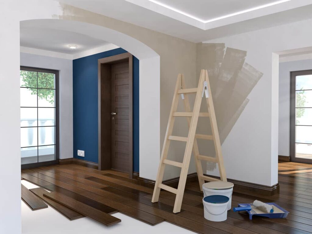 Interior painting setup with a wooden ladder, paint buckets, and partially painted walls in a residential space, illustrating home improvement trends and preparation tips.