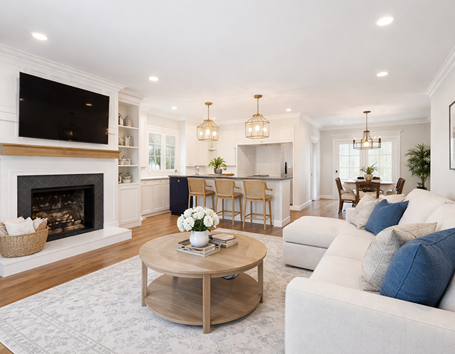 Modern living room with white walls, a cozy sofa, and a round coffee table, featuring a fireplace and open kitchen area, highlighting a stylish and inviting home environment ideal for residential painting services.